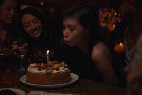 Lachende Gäste bei einer Geburtstagsfeier um eine Torte mit brennenden Kerzen